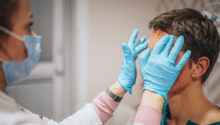 physician wearing blue surgical gloves examining patient's face